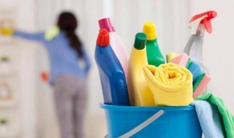 a bucket full of cloth wipes and spray bottles and a woman in the back wiping the wall