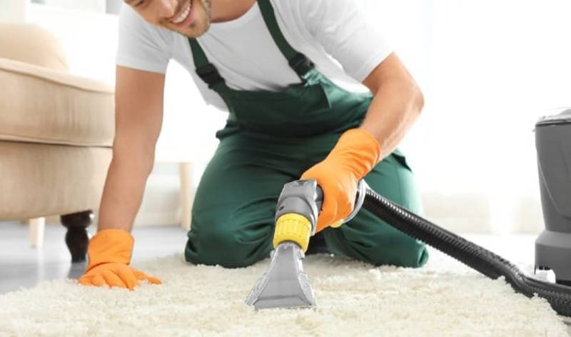 Man in orange gloves vacuuming carpet