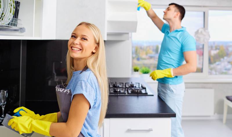 Woman in yellow gloves smiling and a man in blue t-shirt scrubbing behind her
