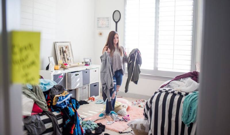 Girl in t-shirt and blue jeans holding some cloths in her hand inside her room