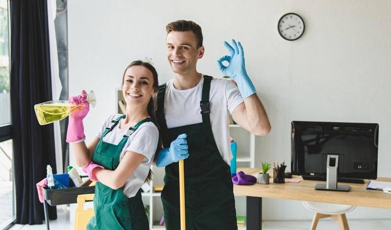 Woman holding bottle and man holding stick both smiling inside a room