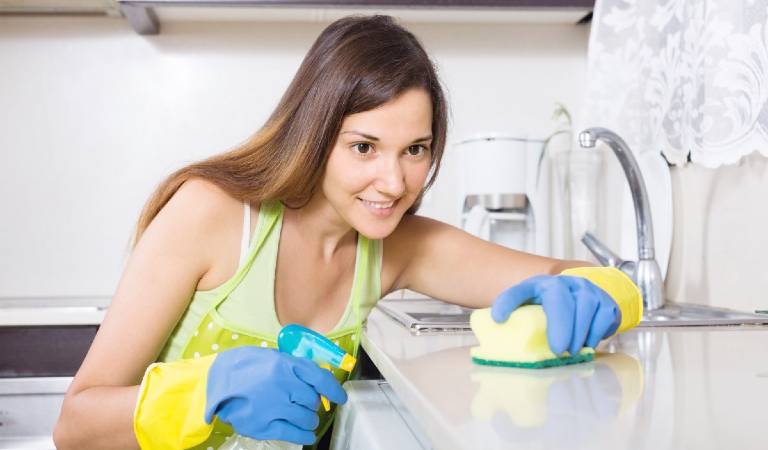 Woman in blue gloves scrubbing marble inside a kitchen