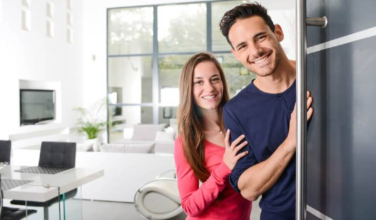 man in black t-shirt and woman in red top welcoming their guest on door