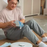 YOUNG MAN WITH A ROBOT VACUUM CLEANER