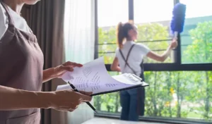 Midsection of woman looking at clipboard against colleague cleaning window