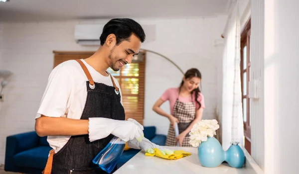 young man and woman cleaning house indoors together happy couple vacuuming messy dirty floor for housekeeping