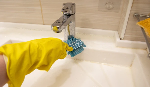 A hand in a yellow glove cleans the sink with a blue brush on the handle. The concept of homework, disinfection
