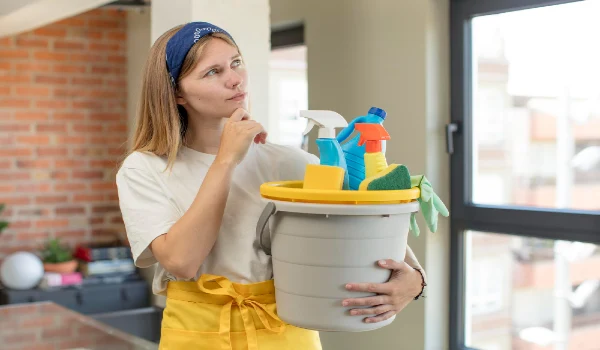 Pretty young woman holding cleaning supplies in a bucket and expressing a concept