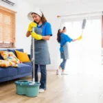 Professional cleaning team wearing aprons and gloves mopping the floor and dusting curtains