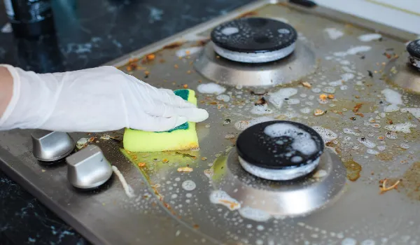Female hand wearing gloves cleaning dirty stove using sponge for washing
