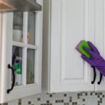 Hand in a purple rubber glove cleaning white kitchen cabinet