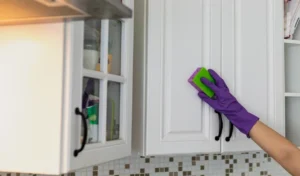 Hand in a purple rubber glove cleaning white kitchen cabinet