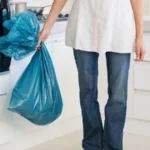 Low section of woman carrying garbage bag in kitchen