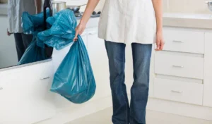 Low section of woman carrying garbage bag in kitchen