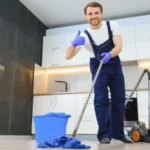 Professional cleaner in blue uniform washing floor and wiping dust from the furniture in the living room of the apartment cleaning service concept