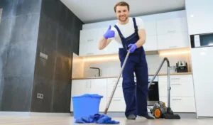 Professional cleaner in blue uniform washing floor and wiping dust from the furniture in the living room of the apartment cleaning service concept