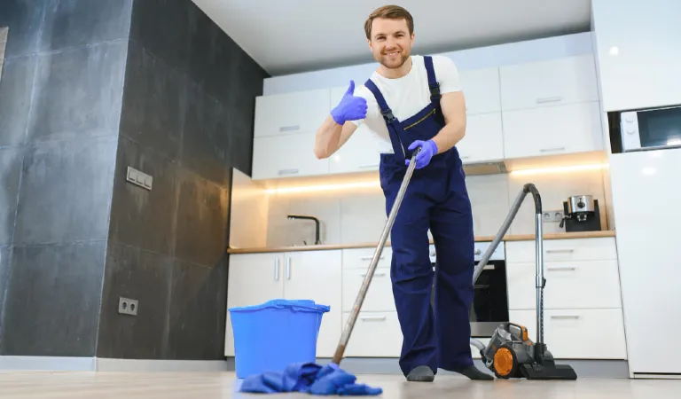 Professional cleaner in blue uniform washing floor and wiping dust from the furniture in the living room of the apartment cleaning service concept