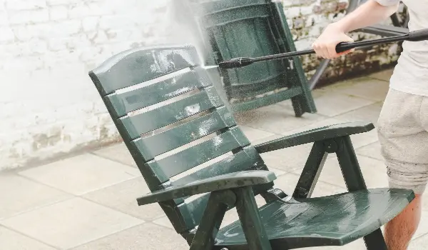 A caucasian guy in gray sweatpants and a tshirt washes plastic dark green sun loungers