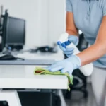 Close up view of woman in protective gloves that cleaning tables in the office