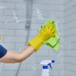 Woman cleaning bathroom washing glass in shower