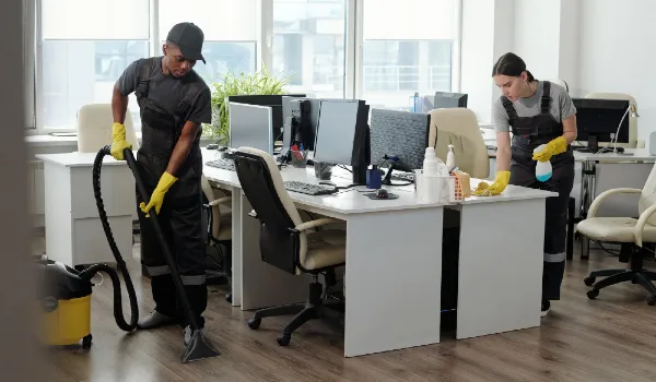Young man and woman using detergent and vacuum cleaner for cleaning openspace office