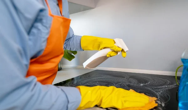 A woman in an apron cleaning the kitchen stove with cleaning products wet cleaning cooking