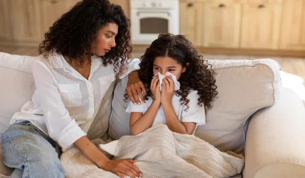 Sad caring mother worries about her sick little daughter sitting near girl on couch