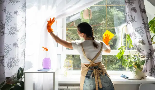 Woman in rubber gloves and apron manually washes window of house with rag cleaner cleanliness in spring cleaning servise